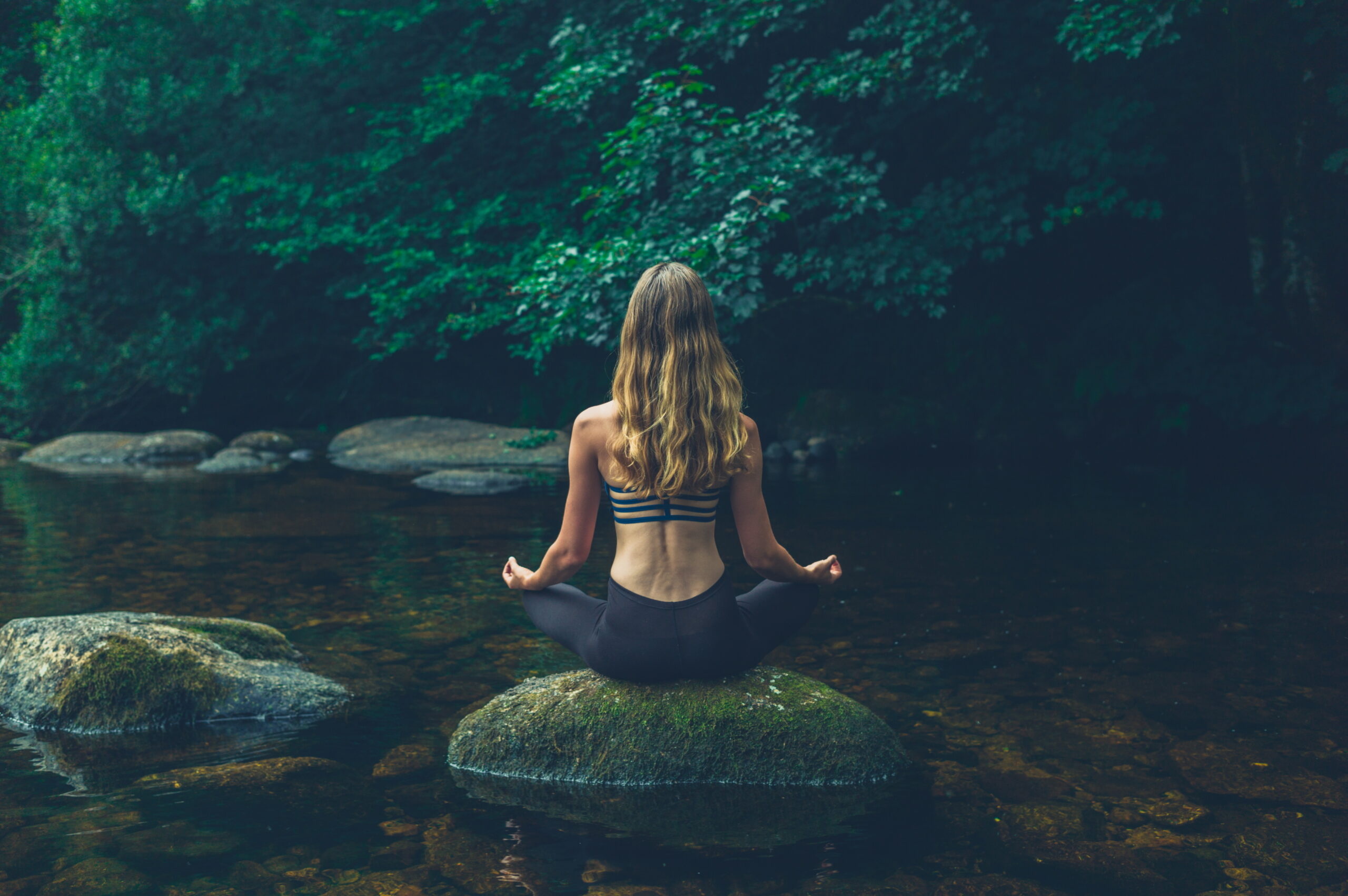 A young woman is meditating on a rock in the river - learn kung fu online