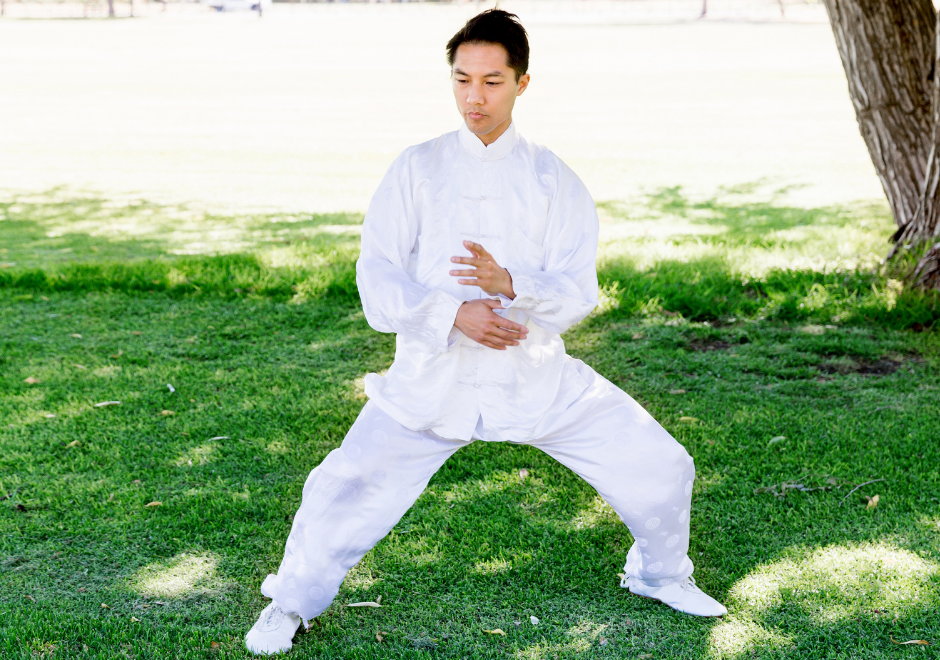 Asian man in white uniform doing Tai Chi in park