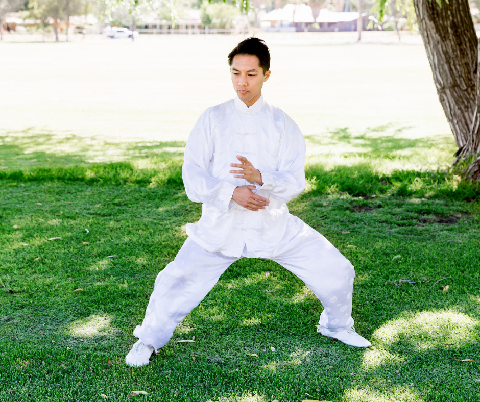 Asian man in white uniform doing Tai Chi in park